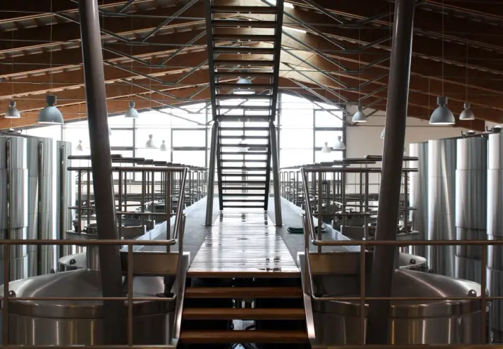 Interno di una cantina moderna con grandi serbatoi d'acciaio e una scala centrale. L'architettura ricorda un progetto di Renzo Cotarella.