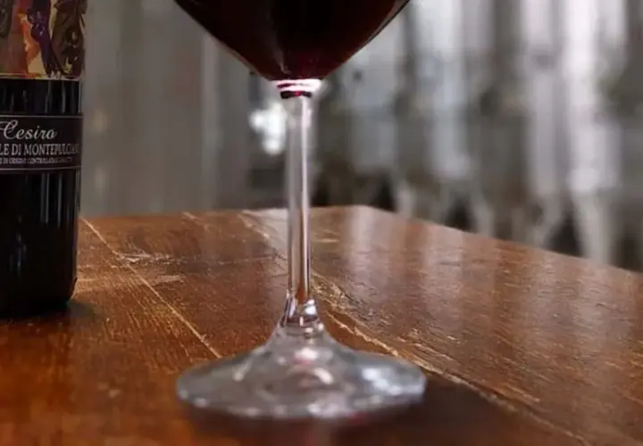 Bottiglie di Vino Nobile di Montepulciano e un calice di rosso, in un'ambientazione che evoca le cantine delle province di Siena.