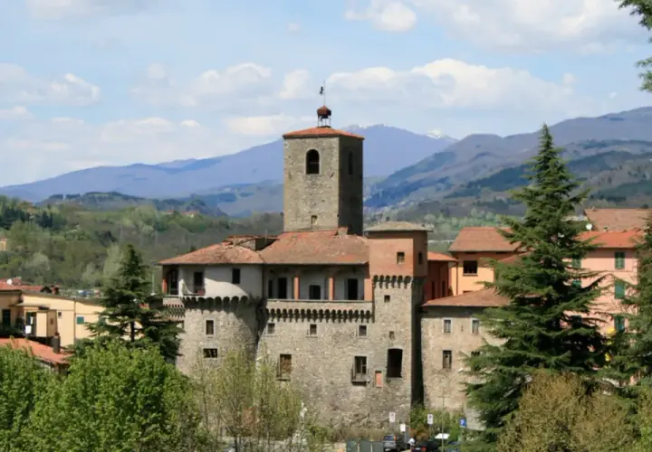 La Rocca Ariostesca domina il borgo con la sua torre imponente, circondata da colline verdi e un cielo azzurro con nuvole bianche.