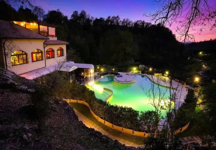Piscina illuminata e un edificio a San Carlo Terme al tramonto, con cielo viola e rosa.
