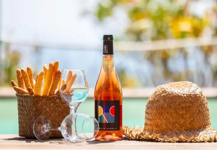 Un bicchiere di vino dolce dell'Elba, grissini croccanti e un cappello di paglia, perfetti per un aperitivo al mare.
