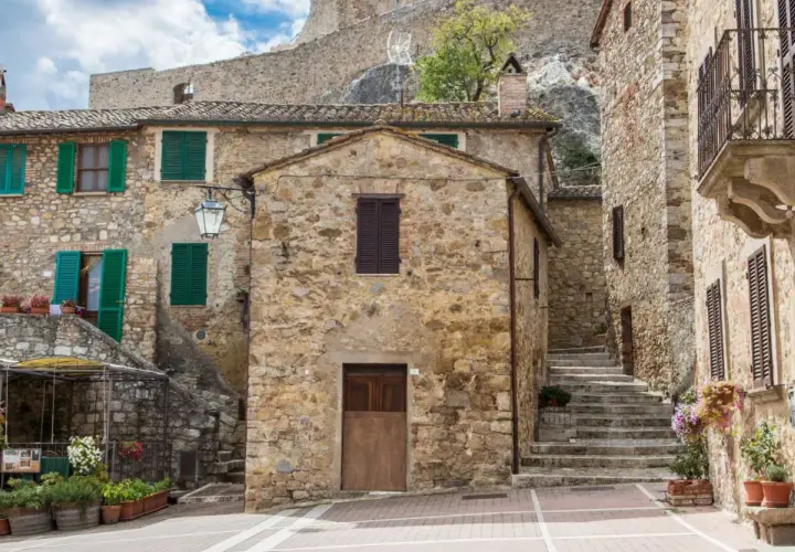 Un vicolo pittoresco a Castel d'Orcia, con case in pietra, persiane verdi e fiori colorati.