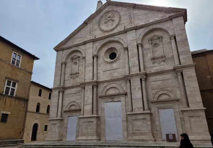 Facciata imponente del Duomo di Pienza, con accanto un edificio in pietra che ricorda il Palazzo Piccolomini.