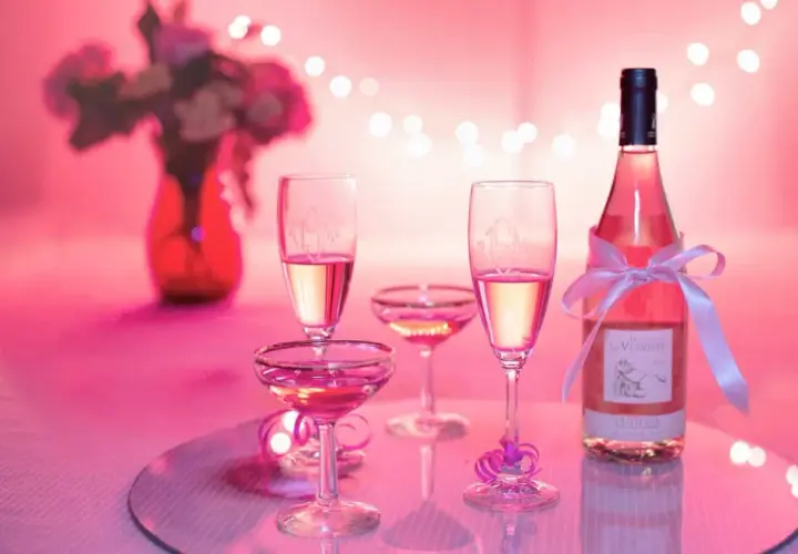 Bottiglia e calici di vino rosato, un brindisi alla vinificazione in rosato, con fiori e luci soffuse.