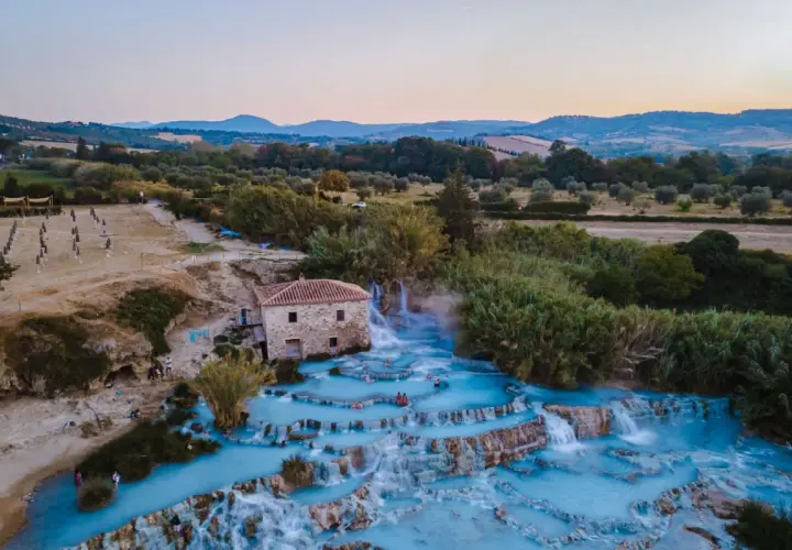 Cascate termali con acqua azzurra e un vecchio mulino, un'oasi di relax che ricorda le terme a Firenze.