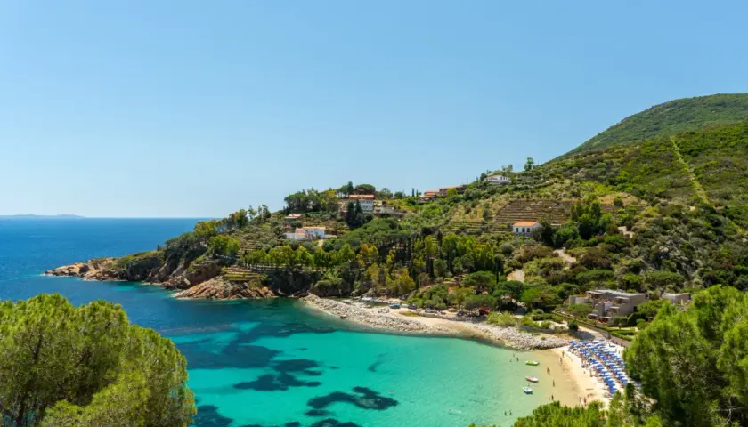 Incantevole baia con acque cristalline, spiagge dorate e case arroccate sulle colline verdi, un sogno di città toscane sul mare.