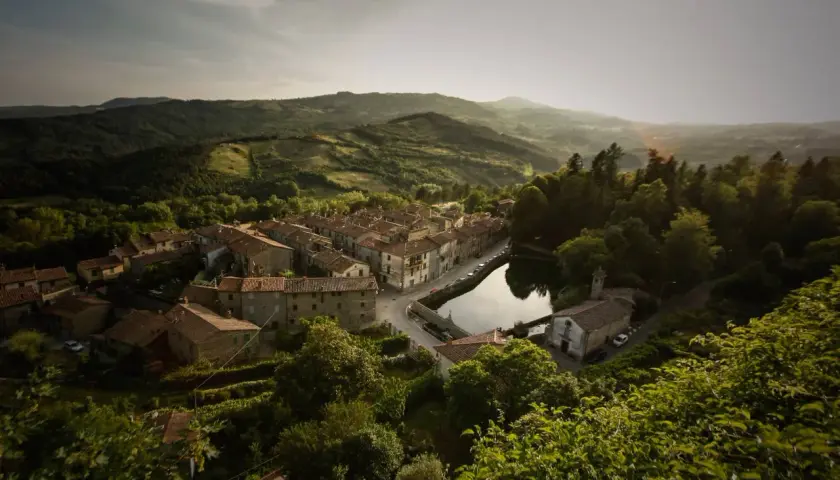 Peschiera Santa Fiora, un borgo toscano incastonato tra colline verdi, con case in pietra e un laghetto che riflette il cielo.