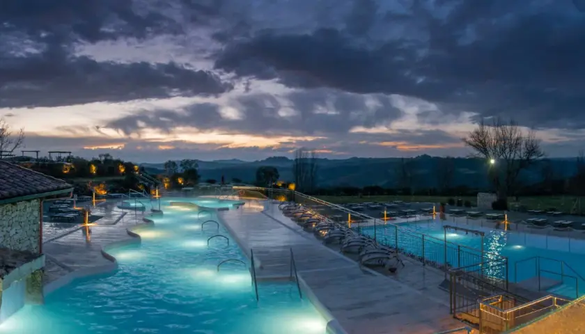 Piscine termali illuminate a Rapolano Terme al tramonto, con un cielo drammatico e colline toscane sullo sfondo.