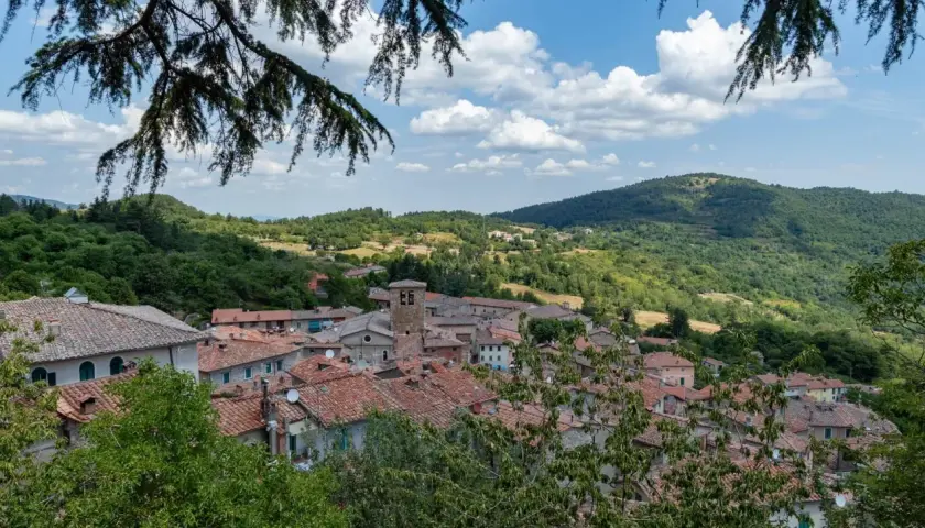 Panoramica di Montieri, Grosseto, con tetti in cotto e colline verdi sotto un cielo azzurro con nuvole bianche.