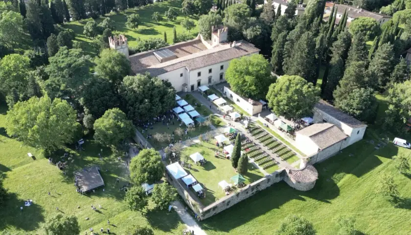 Mercato all'aperto nel parco dell'Acciaiolo, con bancarelle, persone e un edificio storico circondato da alberi.