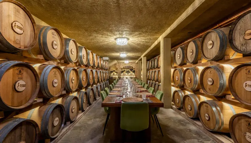 Un'elegante sala per una visita in cantina con degustazione, con botti di legno disposte su entrambi i lati e un lungo tavolo apparecchiato.