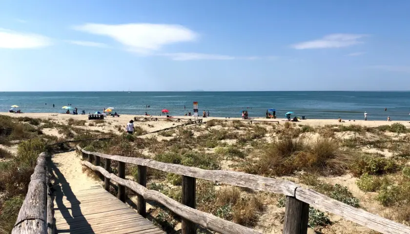 Passerella in legno conduce alla spiaggia di Tirrenia, con bagnanti e ombrelloni sotto il sole. Il mare calmo invita a un tuffo.