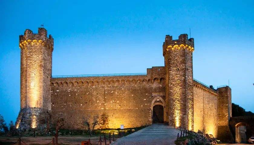 Fortezza illuminata al crepuscolo, un invito a visitare Montalcino e scoprire la sua storia.
