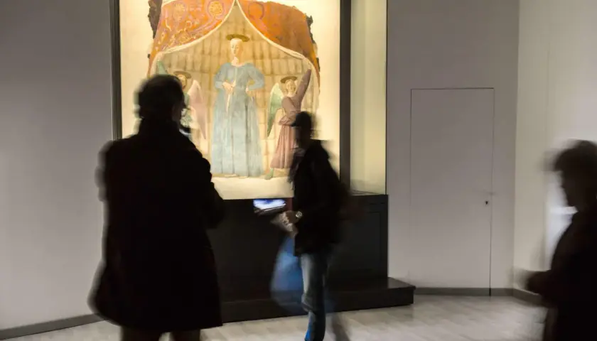 La Madonna del Parto di Piero della Francesca, con visitatori che la ammirano in un museo.