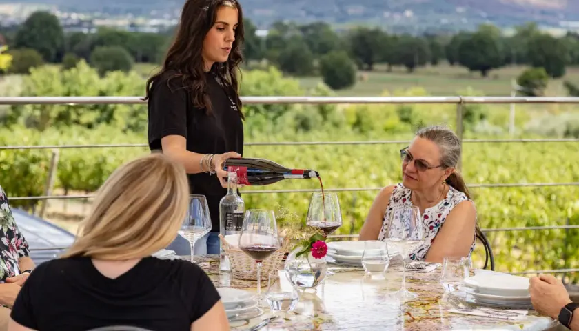 Degustazione di vino alla Baldetti Winery: una giovane donna versa vino rosso in un bicchiere, mentre gli ospiti assaporano il paesaggio.