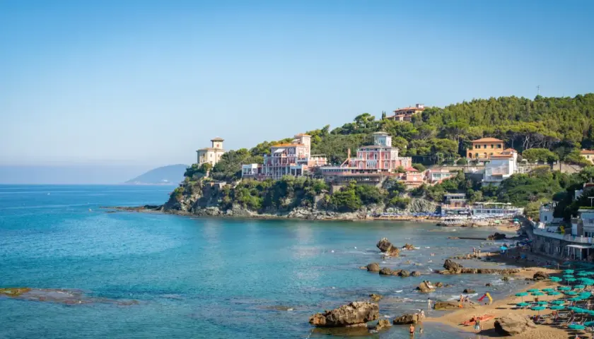 Panorami mozzafiato di Castiglioncello, Italia, con ville storiche affacciate sul mare turchese e una spiaggia animata.