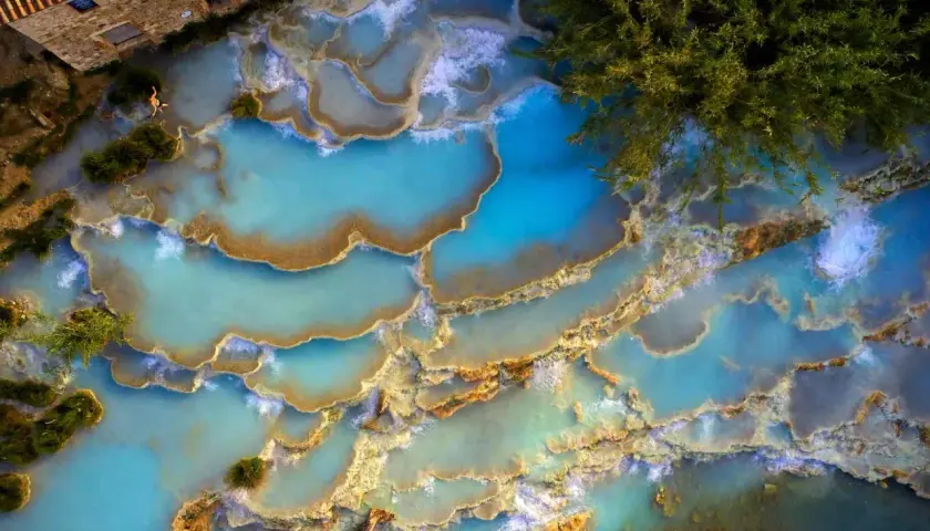 Cascate naturali di acqua turchese in un thermal spa Tuscany, con una persona che si rilassa tra le rocce calcaree.