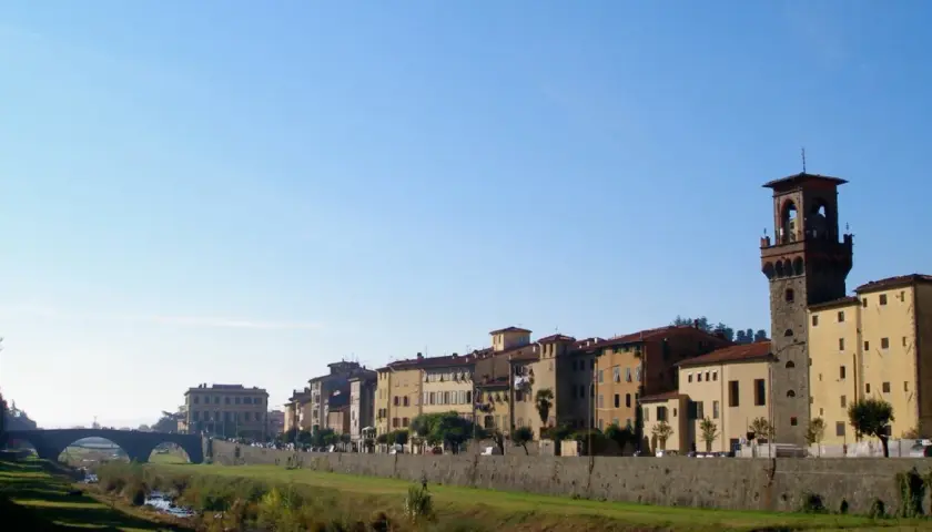 Edifici storici e una torre medievale si affacciano sul fiume nel pescia centro storico, sotto un cielo azzurro.