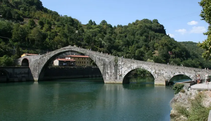 Il Ponte del Diavolo, con i suoi archi in pietra, attraversa un fiume verdeggiante, circondato da colline boscose.