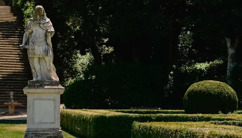 Statua romana domina una scalinata nei **Horti Leonini**. Giardini curati e alberi ombrosi creano un'atmosfera serena.