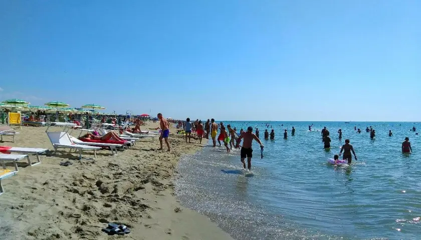 Una giornata di sole a Marina di Tirrenia, con bagnanti che si godono il mare e la spiaggia affollata di ombrelloni e lettini.