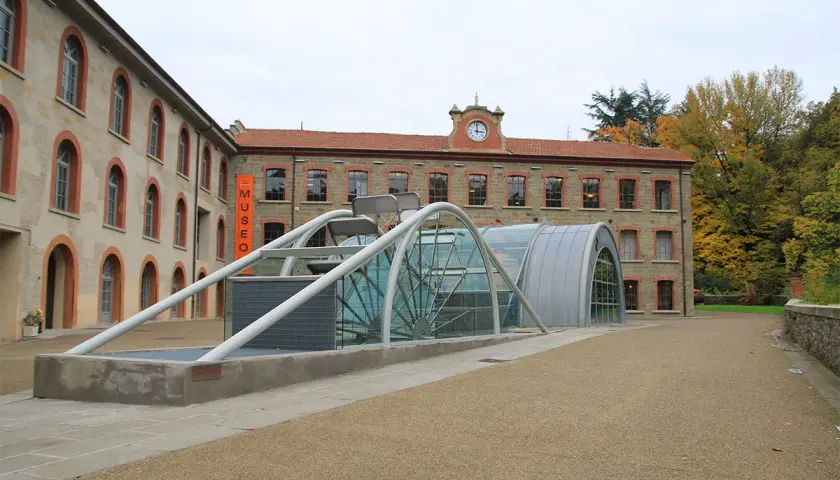 Edificio moderno con struttura in vetro e metallo accanto a un edificio storico, con insegna "MUSEO" a **stia Arezzo**.