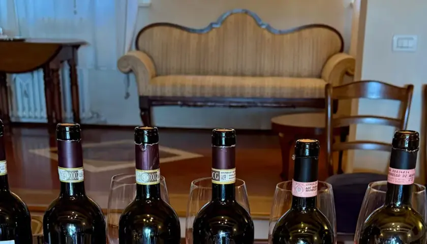 Sei bottiglie di vino, tra cui un **migliore Brunello di Montalcino**, pronte per una degustazione in un salotto elegante.
