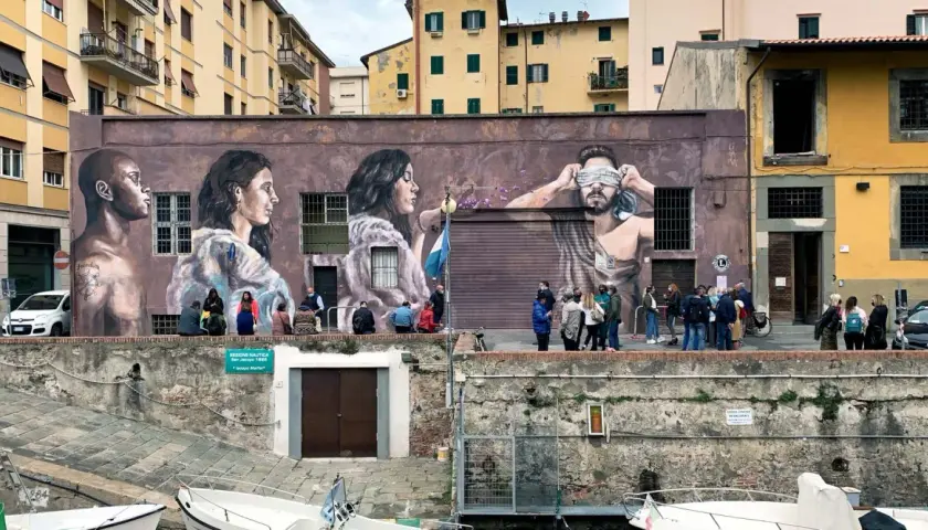 Un imponente murales livornese raffigura tre volti, uno bendato, con persone che osservano l'opera d'arte.