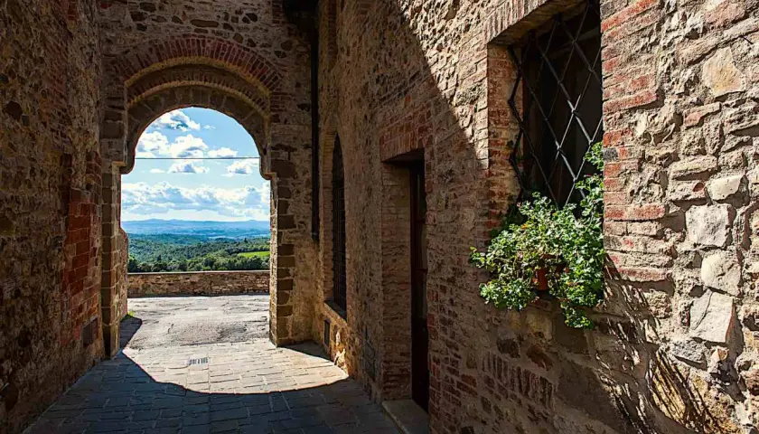 Un vicolo in pietra a San Gusmè, con un arco che rivela un paesaggio collinare toscano.