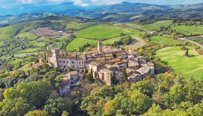 Un borgo toscano arroccato su una collina, circondato da dolci colline verdi e campi coltivati. Un esempio dei borghi toscani più belli.