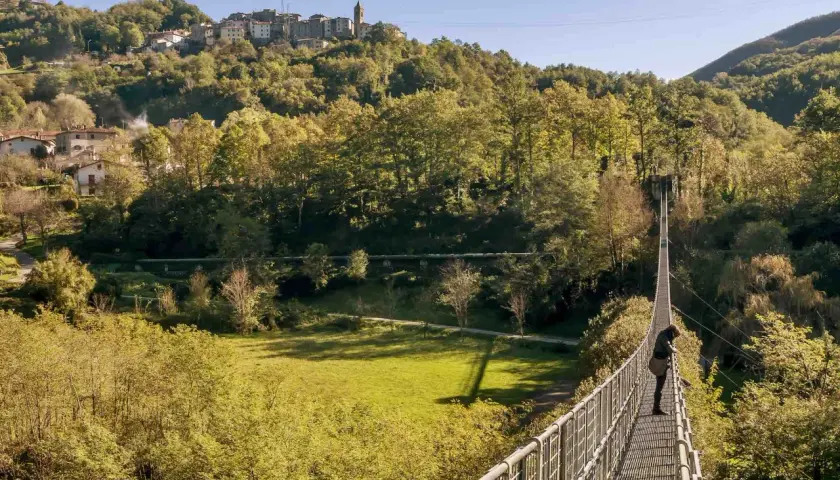 Una persona osserva il panorama dal ponte sospeso delle Ferriere, con un borgo arroccato sulla collina sullo sfondo.