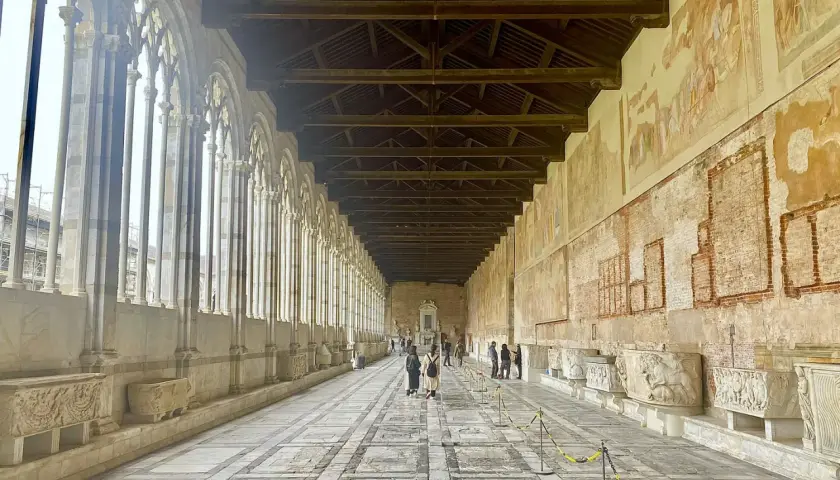 Corridoio del Camposanto Monumentale di Pisa con arcate gotiche, affreschi antichi e sarcofagi romani.