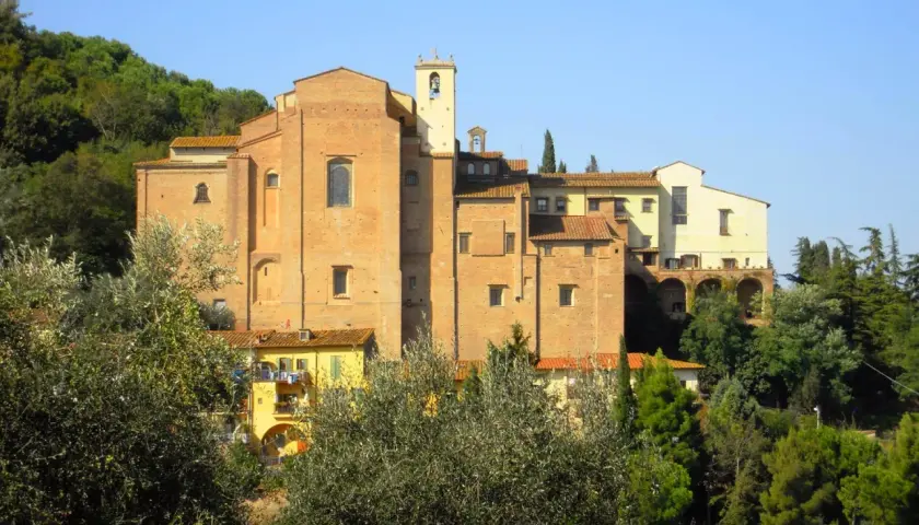Il convento San Francesco a San Miniato, con la sua imponente struttura in mattoni rossi, si staglia tra il verde degli alberi e il cielo azzurro.