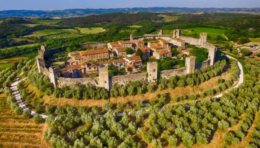 Il centro storico di Monteriggioni, un borgo medievale fortificato, si erge su una collina circondato da mura e torri, immerso nel verde della campagna toscana.