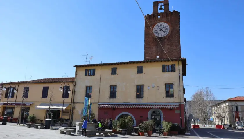Torre dell'orologio in un tranquillo cascina paese, con negozi e gente che passeggia nella piazza.
