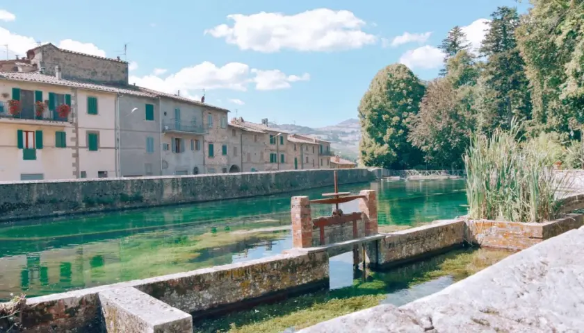 Un canale d'acqua cristallina attraversa un borgo con case antiche, ricordando i pittoreschi **paesi vicini al Monte Amiata**.