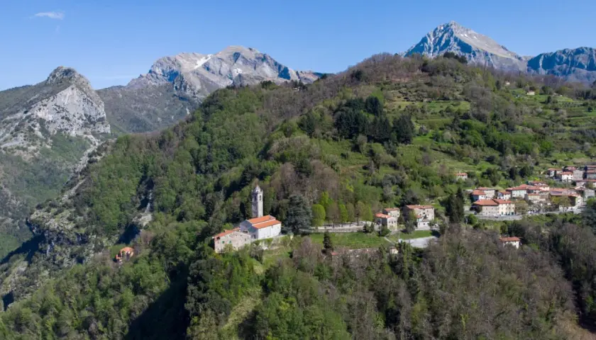 Sant'Anna di Stazzema: un borgo tra monti verdi e cielo azzurro. La chiesa domina il paesaggio, un luogo da scoprire.