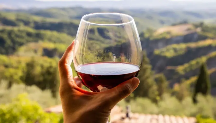 Un bicchiere di vino rosso, forse il miglior Morellino di Scansano, con un panorama collinare toscano sullo sfondo.
