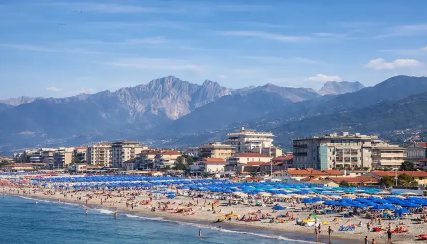 Una vivace spiaggia libera al Lido di Camaiore, con montagne imponenti sullo sfondo e un mare azzurro.