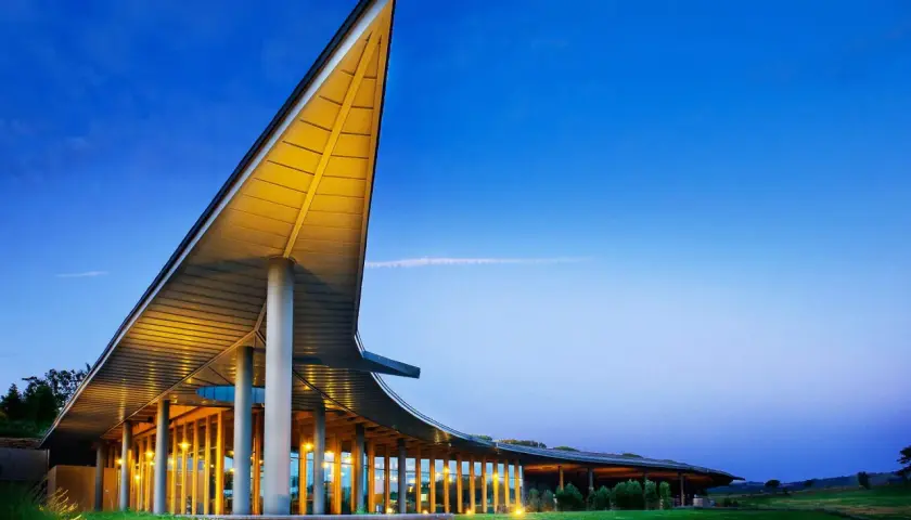 La tenuta ammiraglia Frescobaldi, con la sua architettura moderna illuminata, si staglia contro il cielo serale. Le recensioni lodano questo luogo.