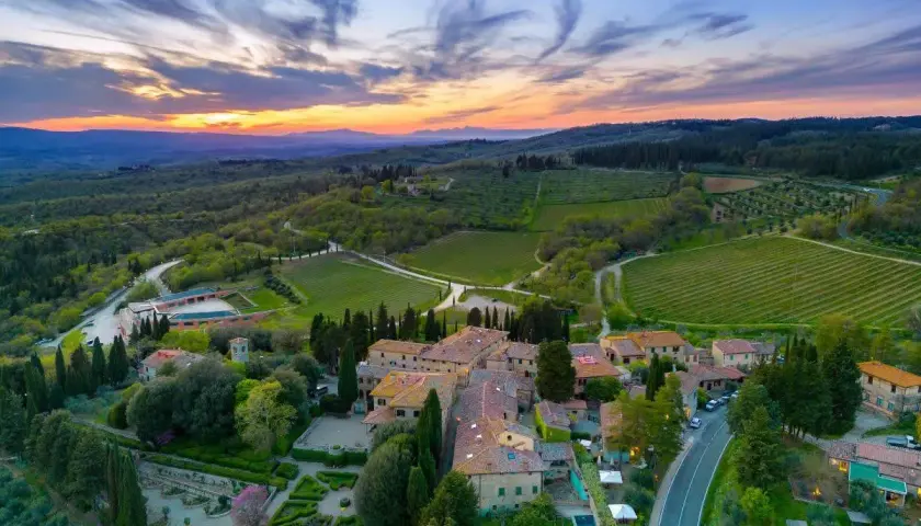 Tramonto mozzafiato sulla **chianti region**, con vigneti rigogliosi e un borgo toscano che si illumina sotto il cielo colorato.