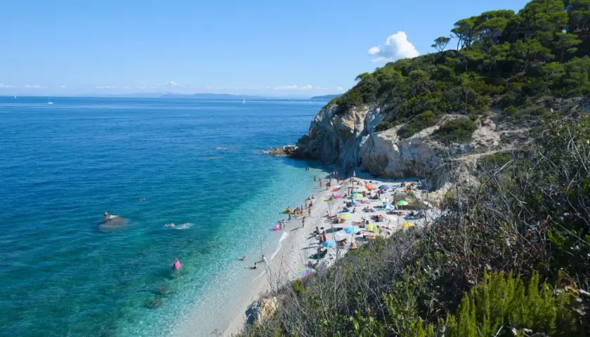 Spiaggia affollata vicino a Campiglia Marittima, con gente che prende il sole e nuota nelle acque cristalline.