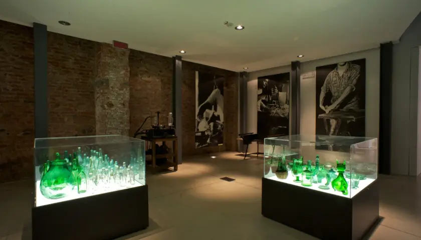 Vetrina con bottiglie verdi illuminate, un'esposizione che racconta cosa vedere a Empoli, tra storia e arte del vetro.
