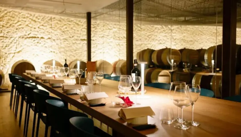 Tavola apparecchiata in una cantina dei vini, con botti sullo sfondo.