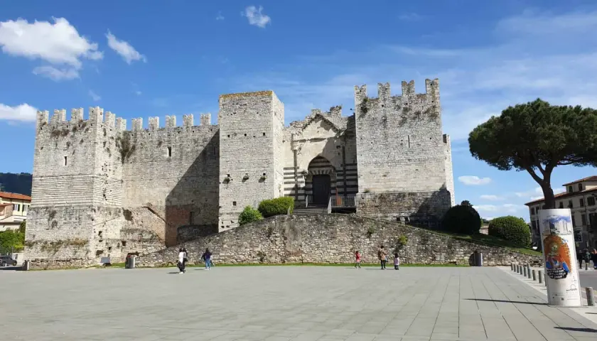 Castello medievale nel prato centro storico, con un grande albero e cielo azzurro.
