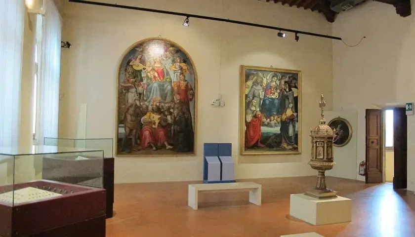 Interno di una sala dei musei di Arezzo con dipinti rinascimentali, un'urna e teche espositive.