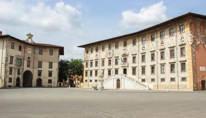 La **piazza dei Cavalieri** a Pisa, con i suoi palazzi storici e la scalinata monumentale, sotto un cielo nuvoloso.