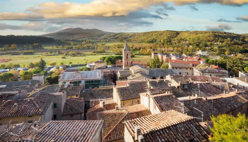Panoramica di Sarteano cosa vedere: tetti in cotto, campanile e colline verdi sotto un cielo nuvoloso.