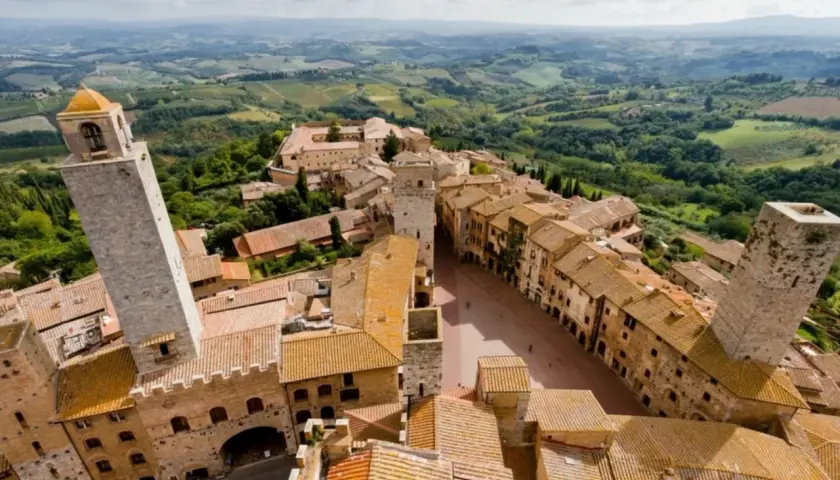 Panoramica aerea di San Gimignano, con le sue torri medievali che svettano tra i tetti di tegole rosse. Un paesaggio incantevole, tipico dei borghi vicino San Gimignano, immerso nel verde delle colline toscane.