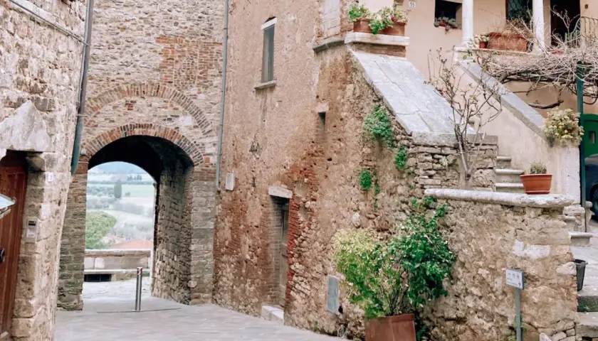 Antico vicolo con arco in pietra, tipico dei borghi vicino Rapolano Terme. Scale in pietra e piante in vaso aggiungono fascino.